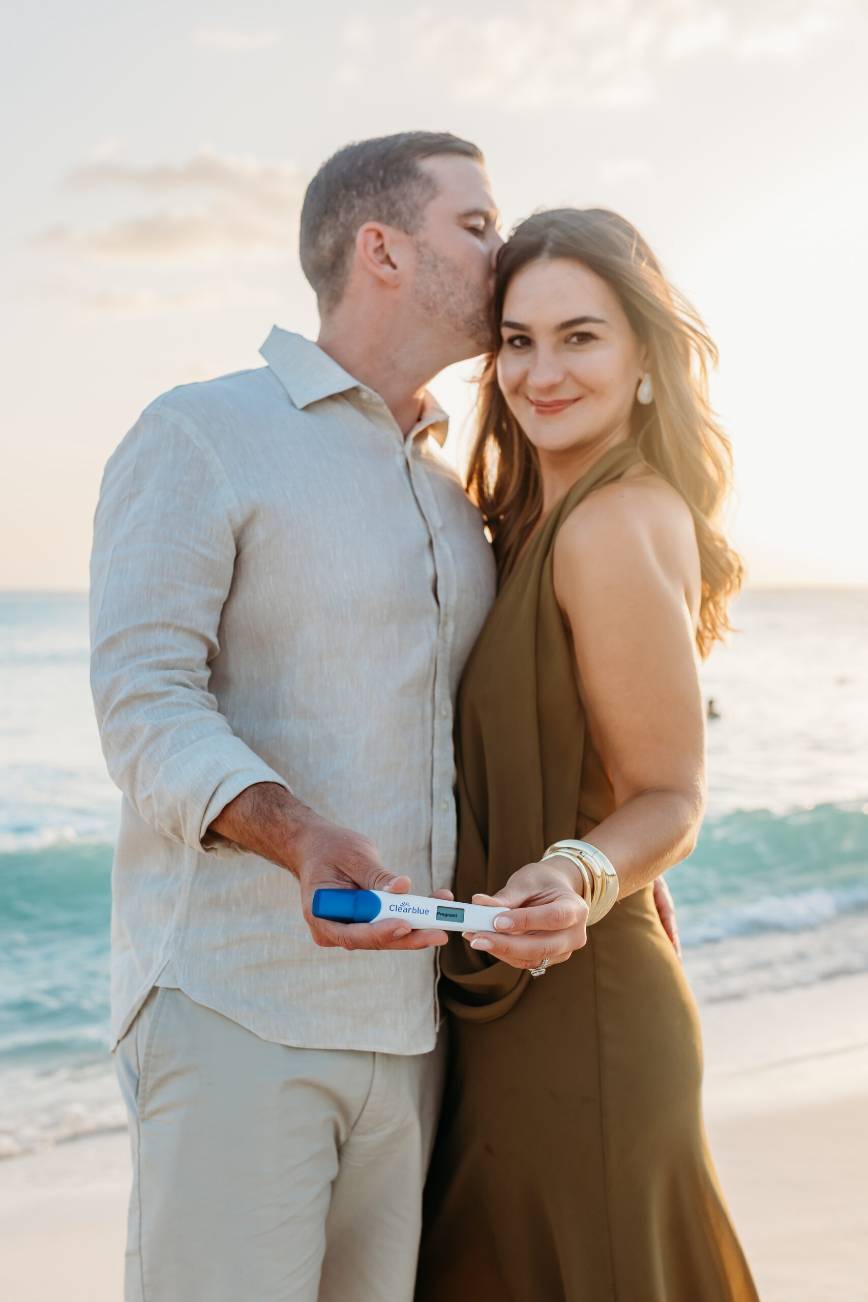 Maternity photographer La Romana captures a happy couple on a sunset beach, announcing a pregnancy with a positive Clearblue test. Perfect for destination portraits.