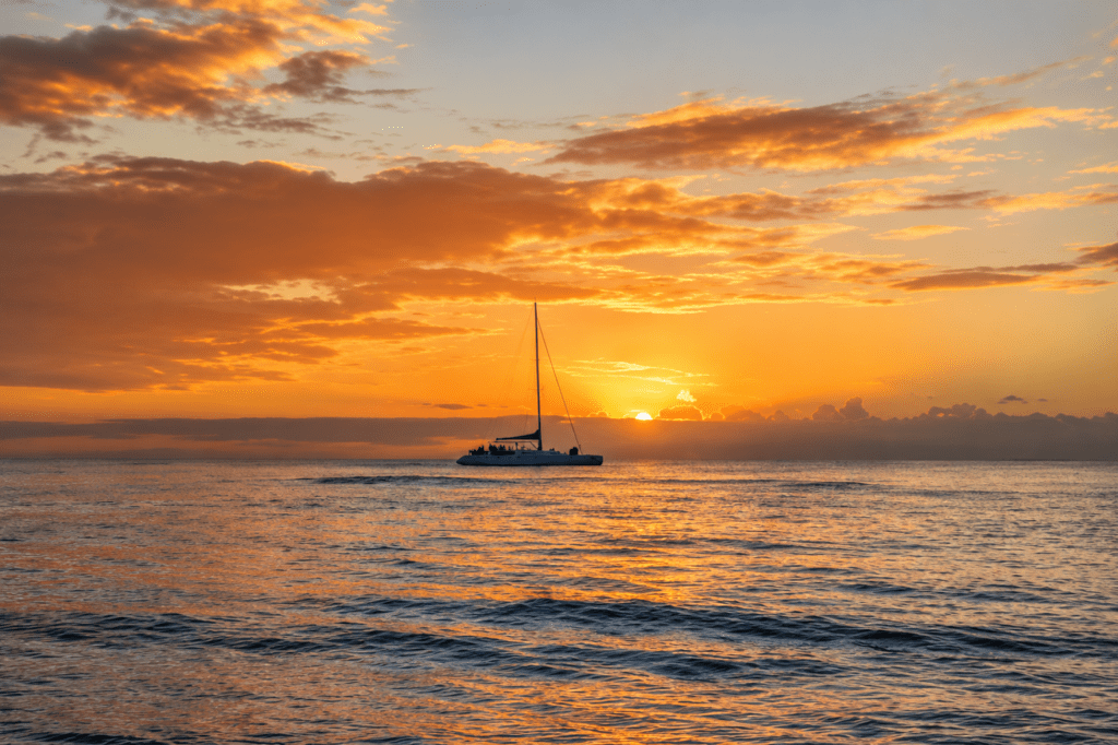 Large catamaran sailboat silhouetted on a vast, golden Caribbean ocean at sunset, ideal for an adventurous destination baby moon and portrait photoshoot by a La Romana photographer.