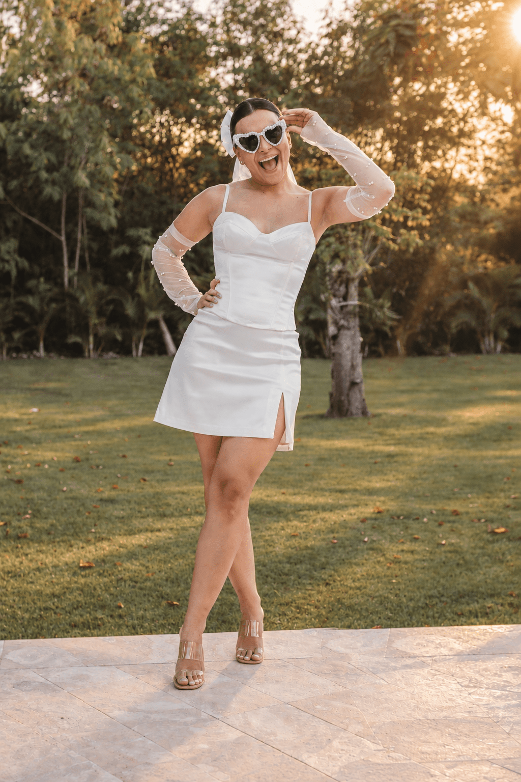 Playful bride-to-be wearing heart-shaped sunglasses, a veil, and a short white dress during a bachelorette party photoshoot in Cap Cana, captured by a La Romana photographer.