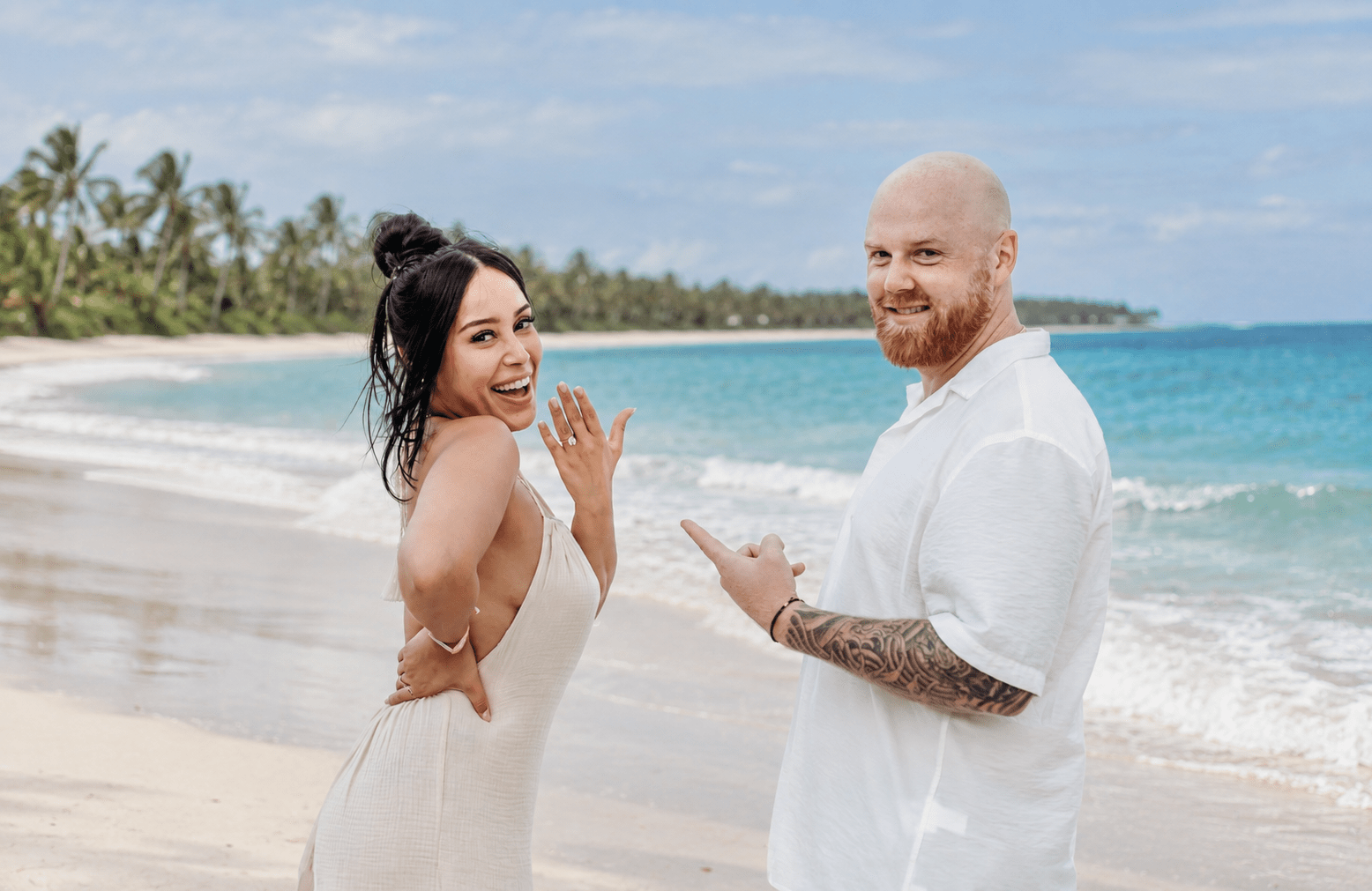 Excited newly engaged woman showing off her engagement ring while her partner points at it on a white sand beach in Miches, captured during a proposal photoshoot by a La Romana photographer.
