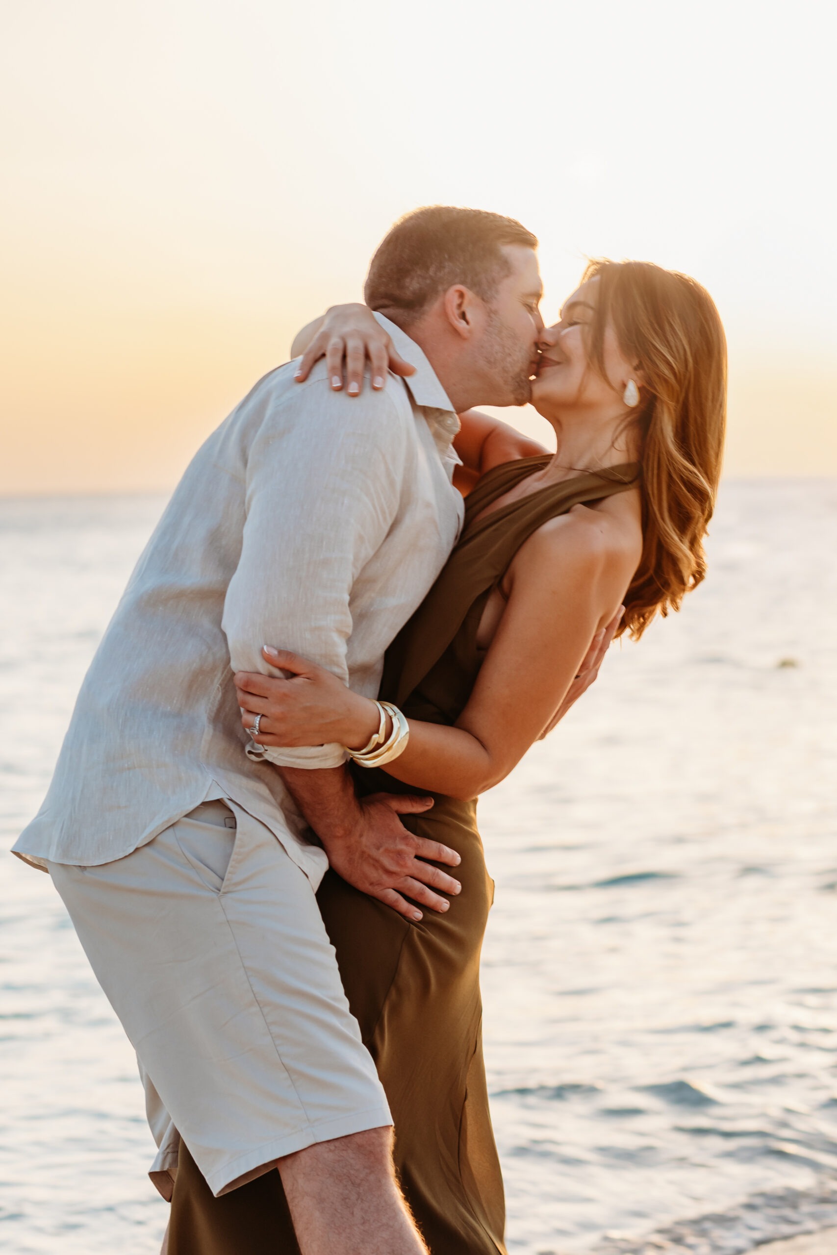 Expectant couple kissing in a romantic embrace on the beach at golden hour during a maternity photoshoot at Secrets La Romana, captured by a La Romana photographer.