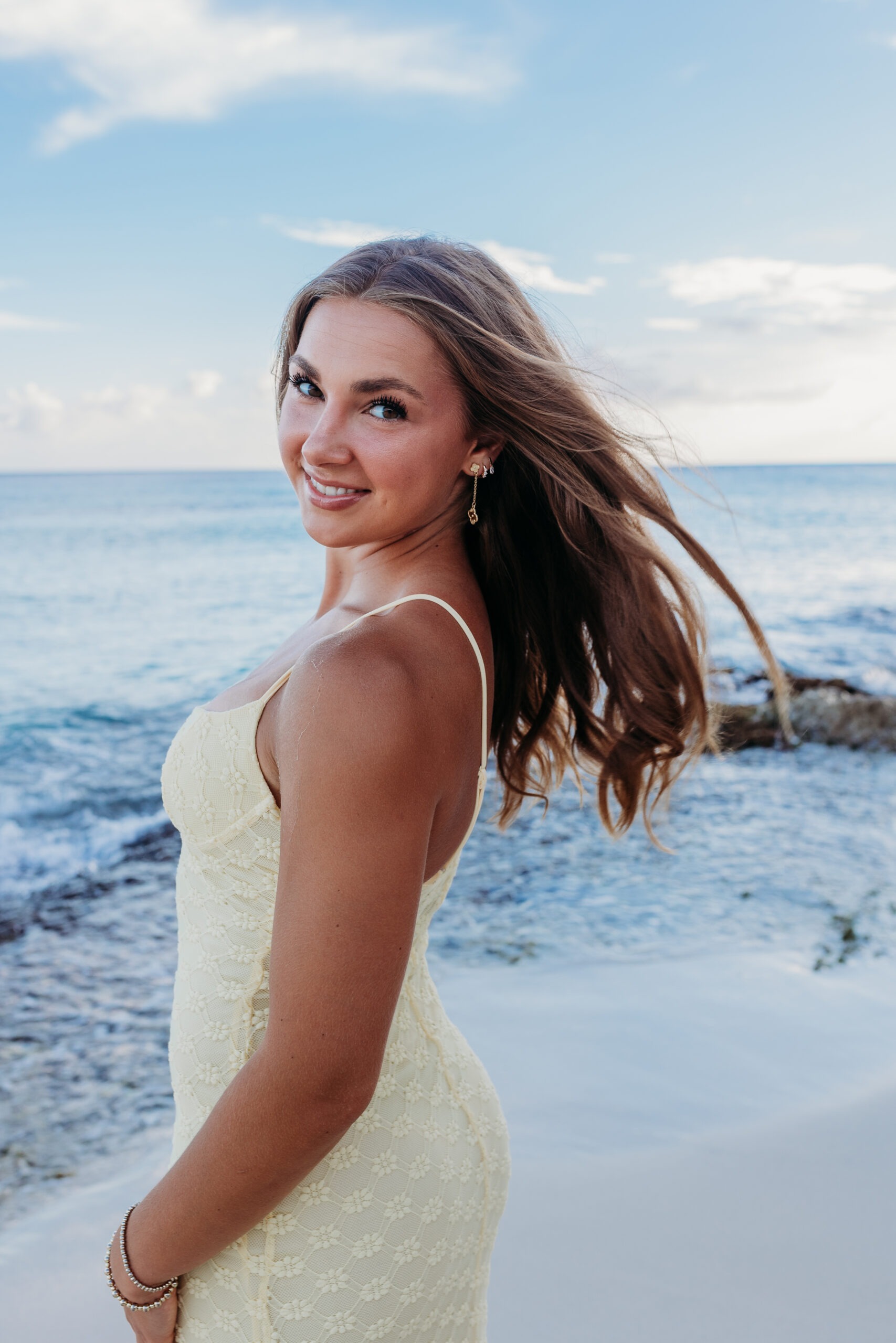 Young woman smiling over her shoulder in a light yellow dress during a solo beach photoshoot in Miches, captured by a La Romana photographer in the Dominican Republic.
