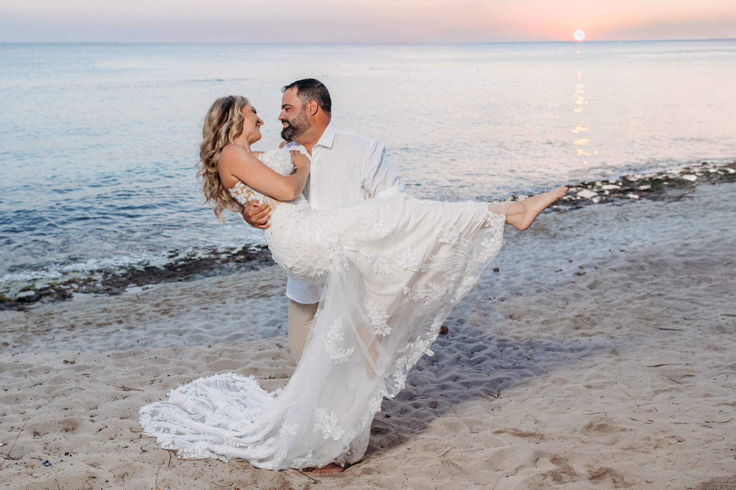 Groom holding his bride in a romantic embrace on the sandy beach during a sunset vow renewal ceremony at Dreams Dominicus La Romana in Bayahibe, photographed by a La Romana photographer.