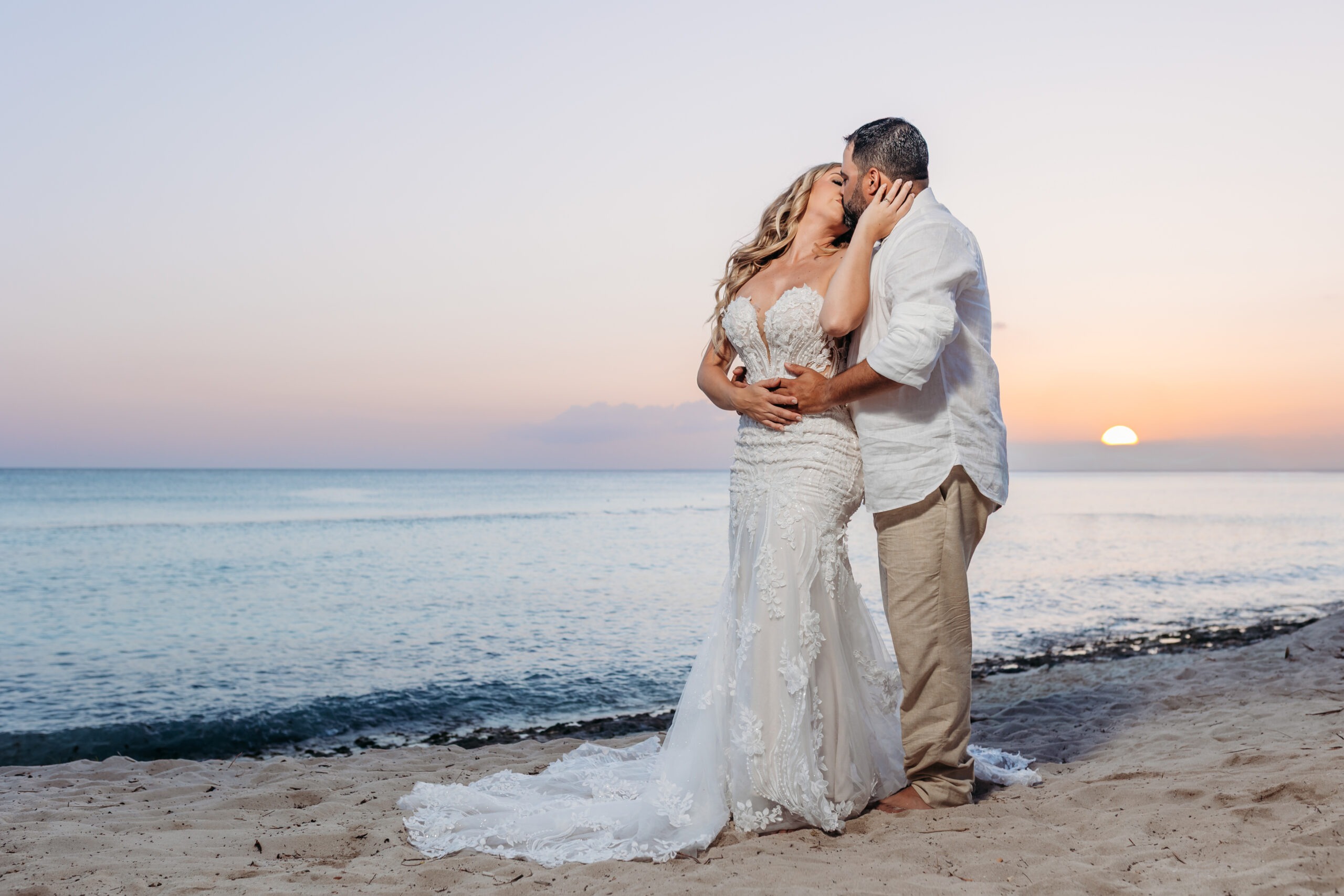 Romantic bride and groom kissing on the sandy shore at sunset during a beach vow renewal ceremony at Cadaqués Caribe in Bayahibe, captured by a La Romana photographer.